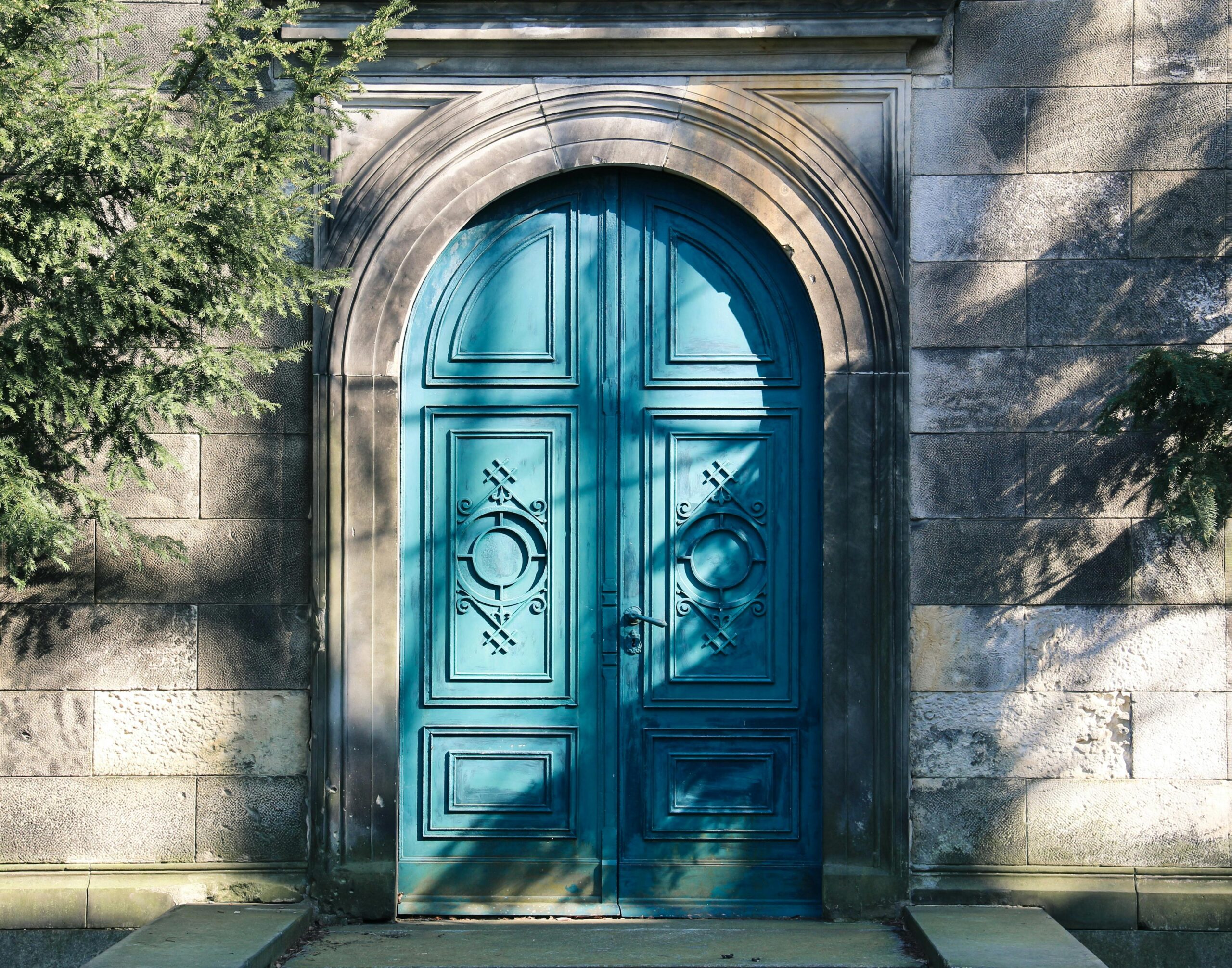 A vibrant blue arched door with gothic designs. Shadows of trees add depth.